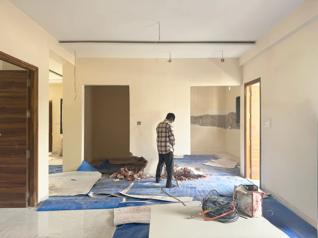 Apartment mid-renovation in Hyderabad, bare unpainted walls, plastic floor sheeting and debris during fit-out