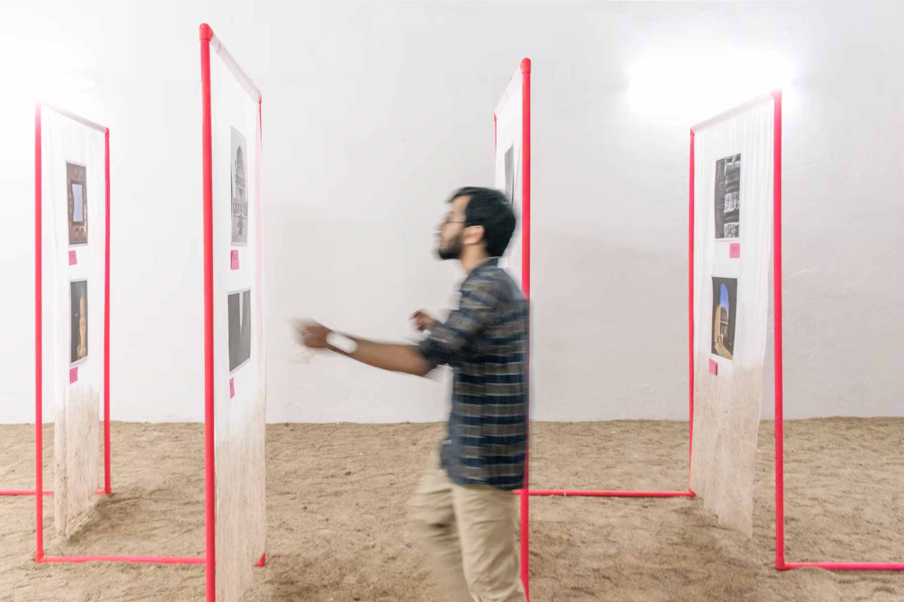 Photo-art installation: a visitor walks among red-framed translucent panels of heritage photographs over a sand floor