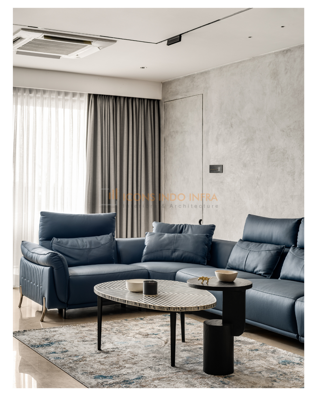 Living room in Hyderabad with deep-blue leather sofa, microcement wall, grey drapes and an oval stone coffee table