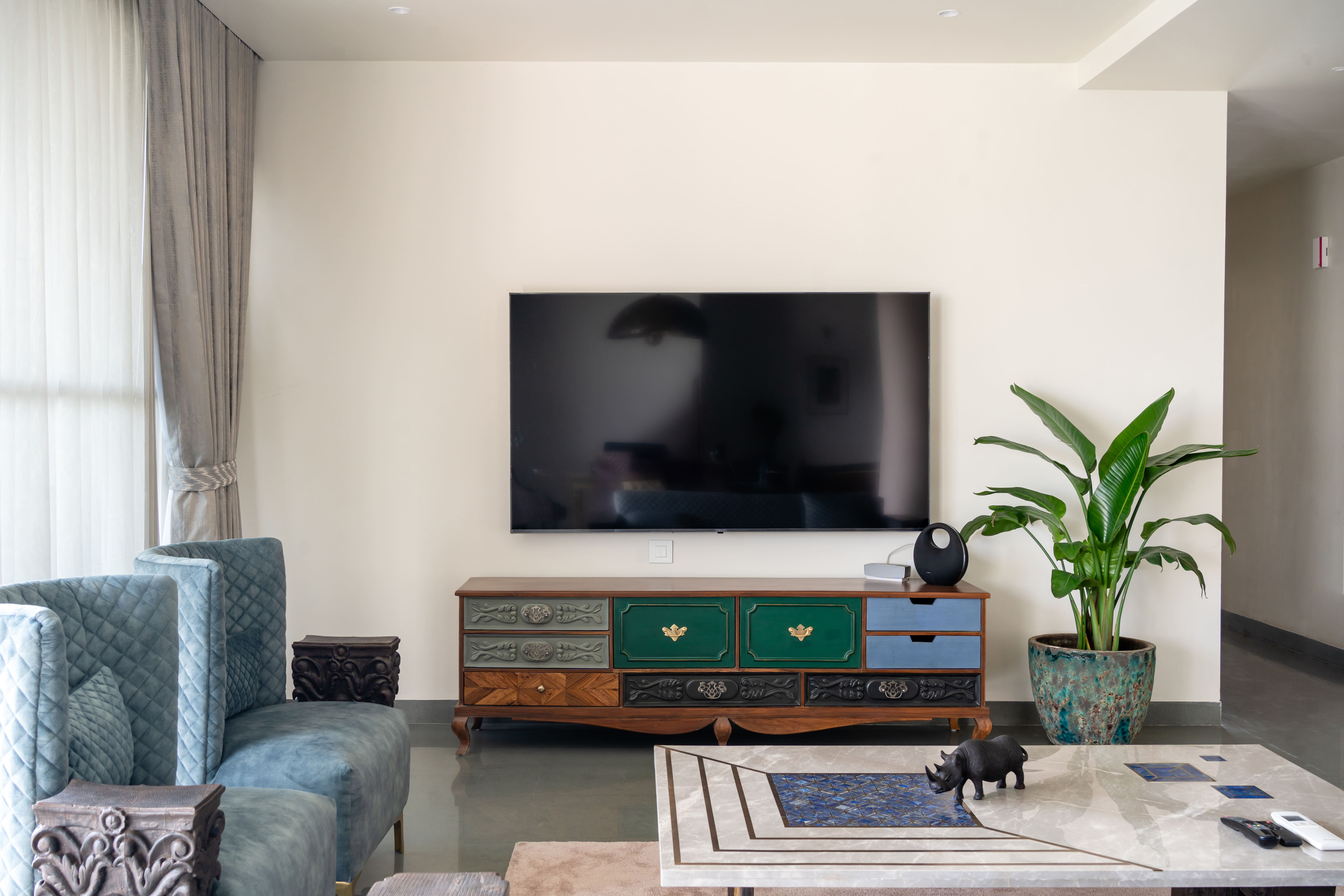 Living room TV wall above a green-and-blue hand-painted antique console with a potted plant and marble table, Hyderabad