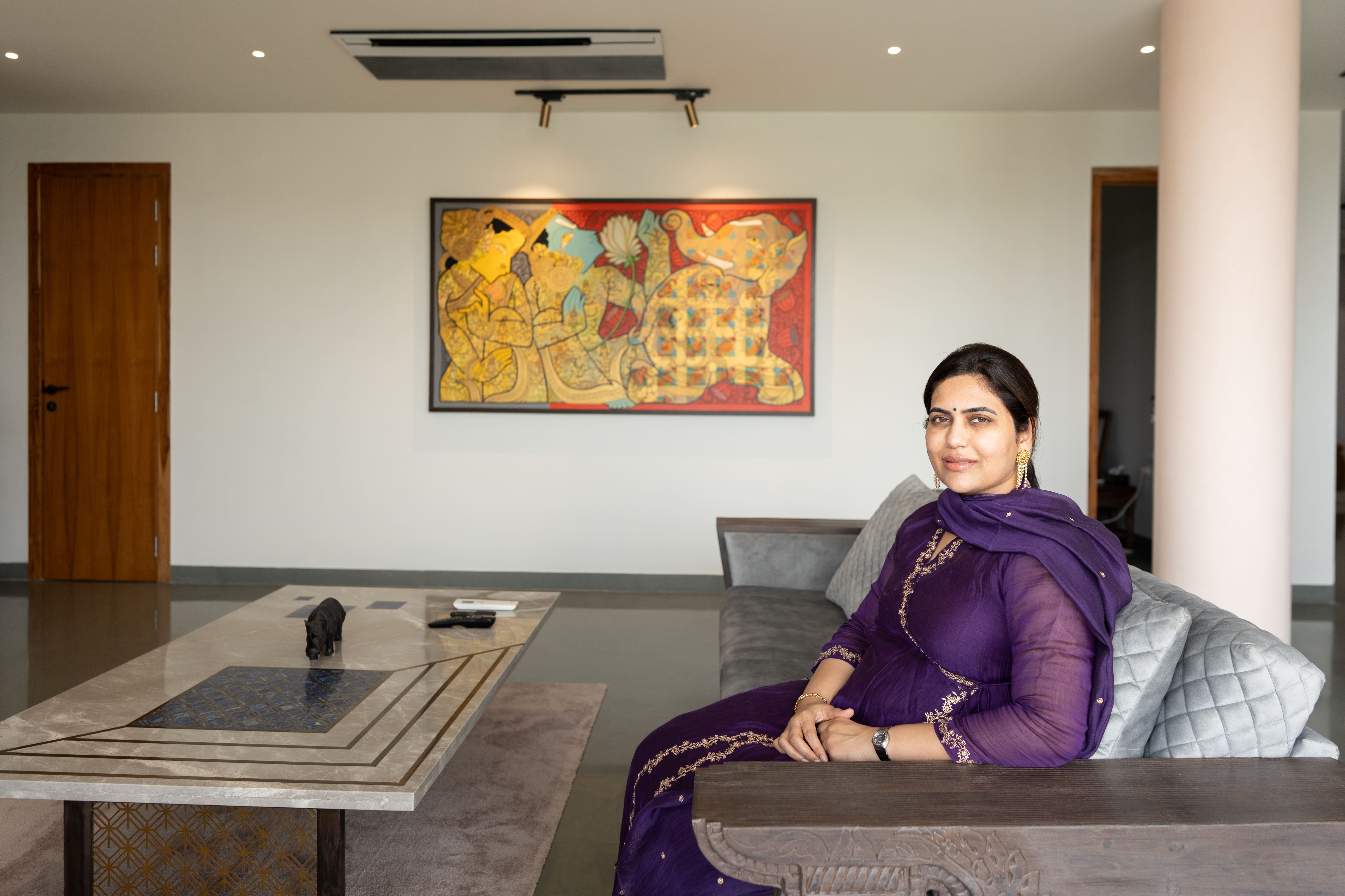 Homeowner in a purple salwar suit seated on a grey sofa beneath a colourful abstract painting in a Hyderabad living room