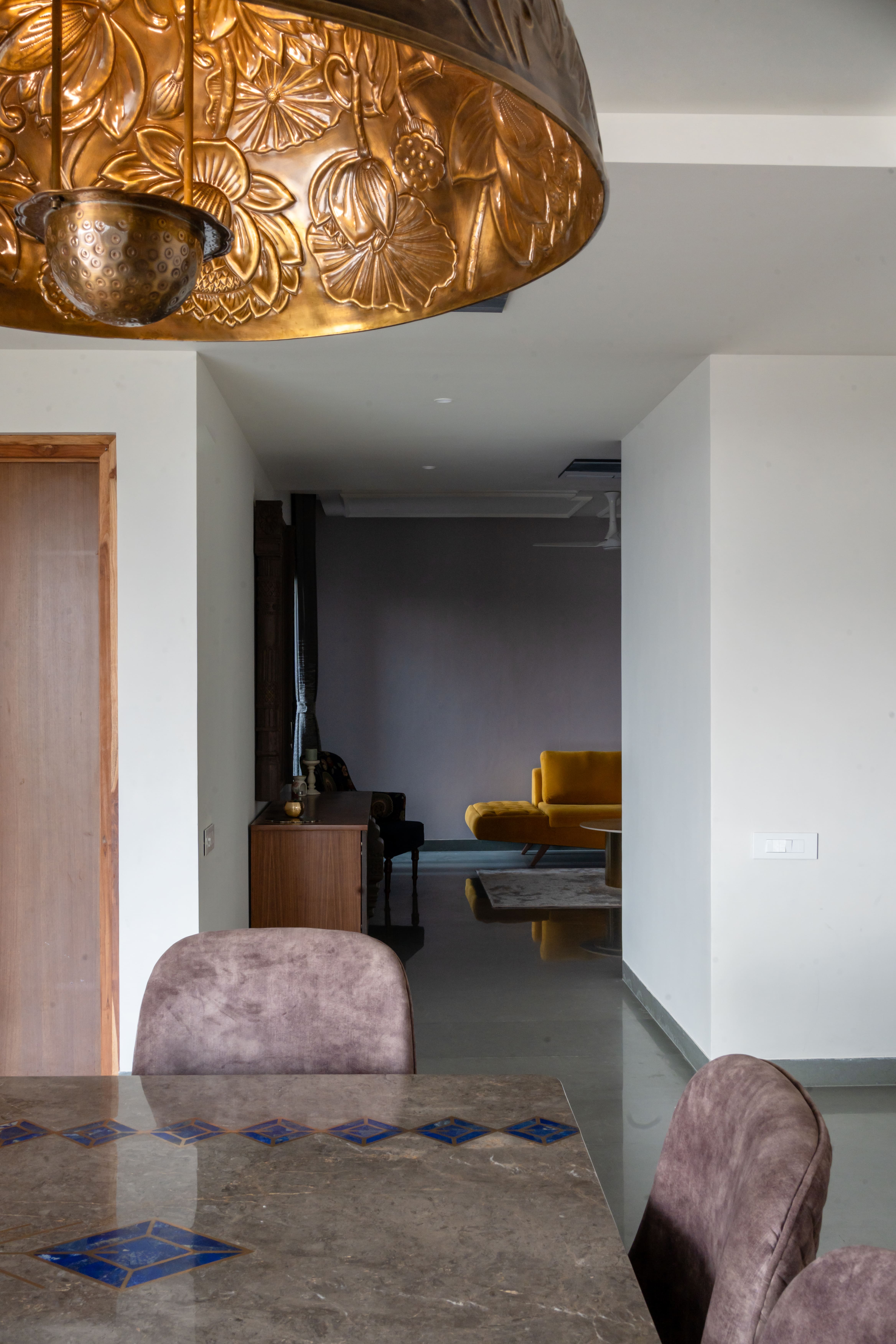 Dining nook in Hyderabad with embossed copper lotus pendant, brown marble table with blue inlay and mauve velvet chairs