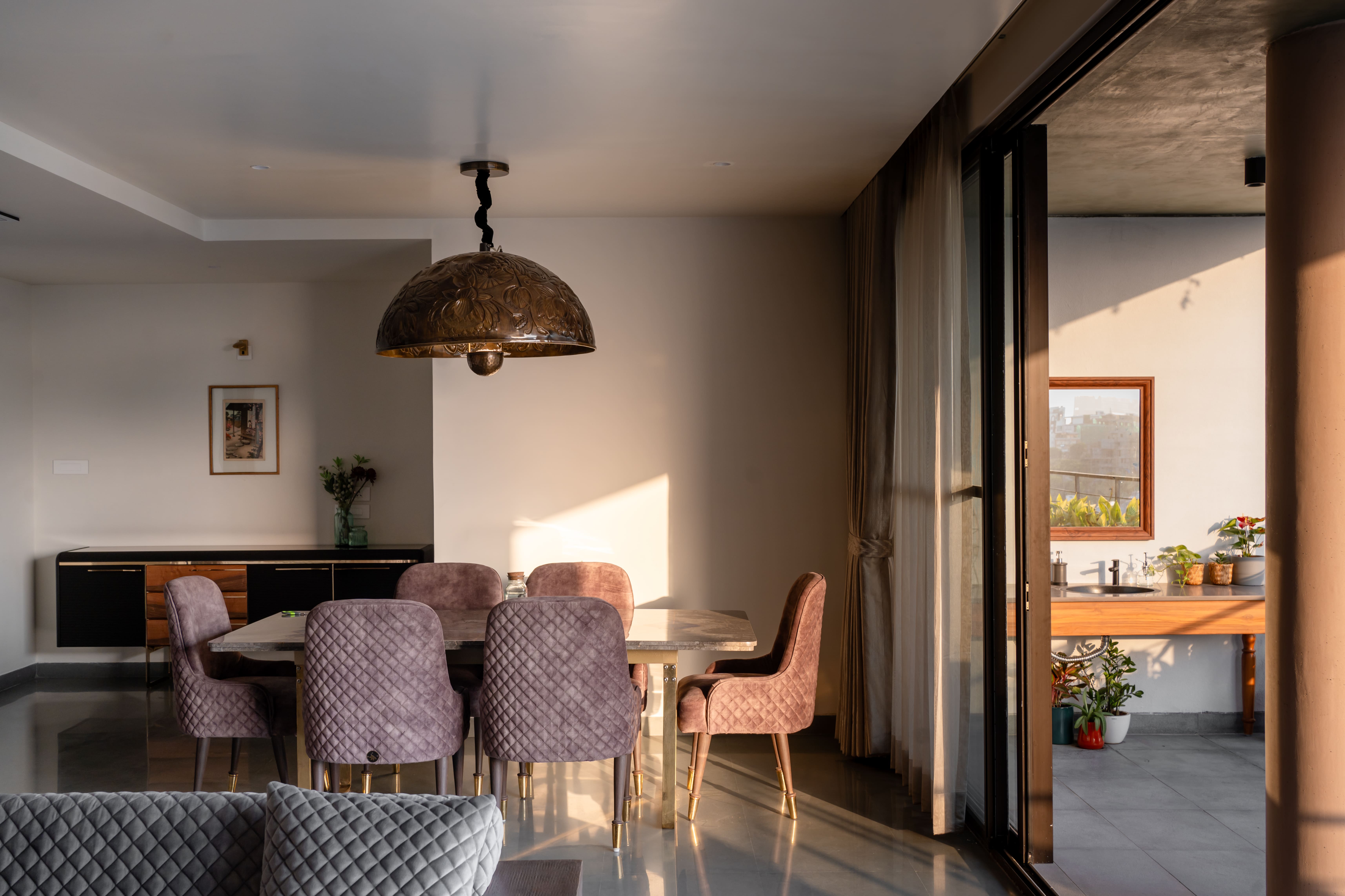 Open dining space, Hyderabad with mauve velvet chairs, copper dome pendant and sliding glass doors opening to a balcony garden