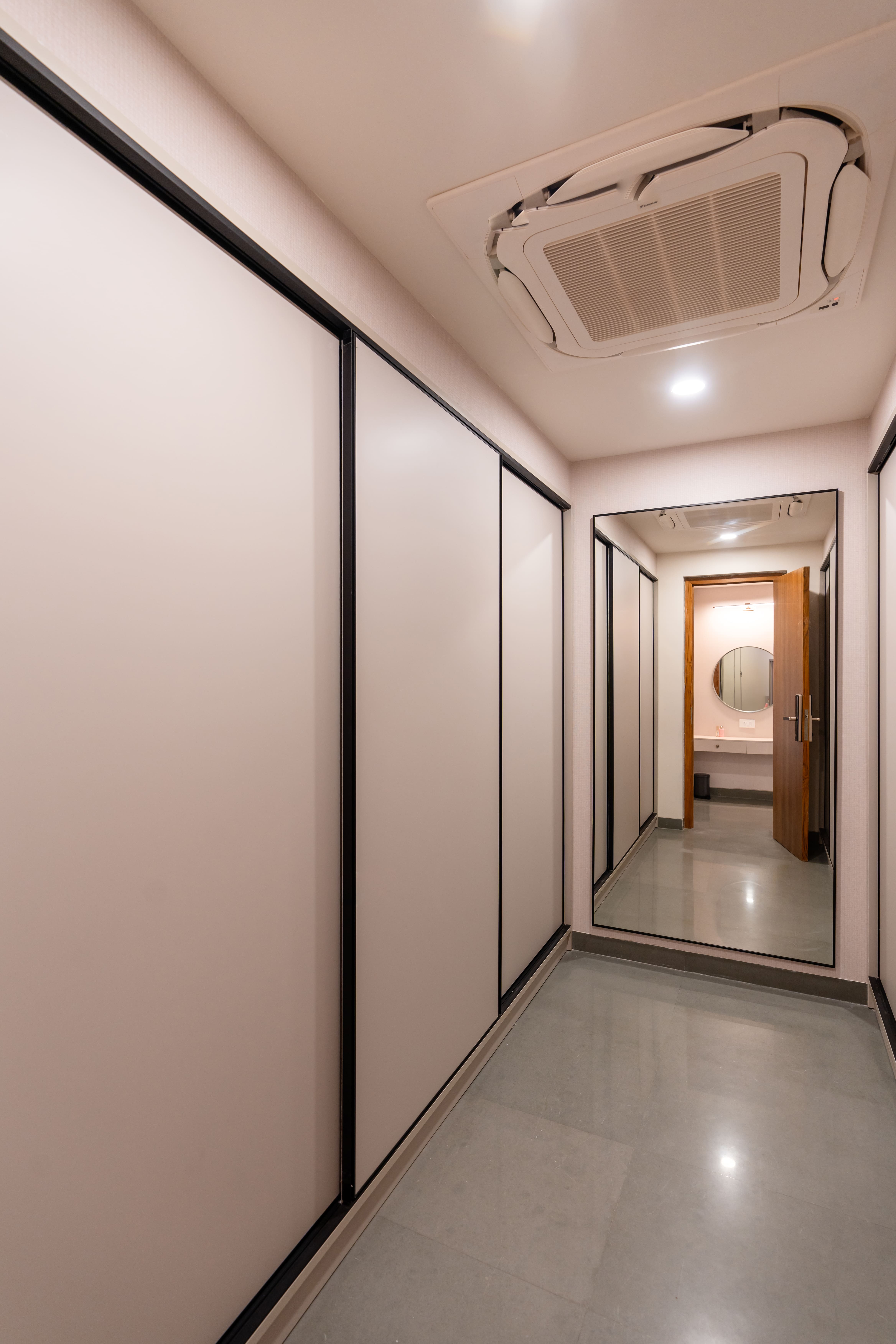Master bedroom walk-in wardrobe corridor with white sliding shutters, black-framed full-length mirror and cassette AC, Hyderabad