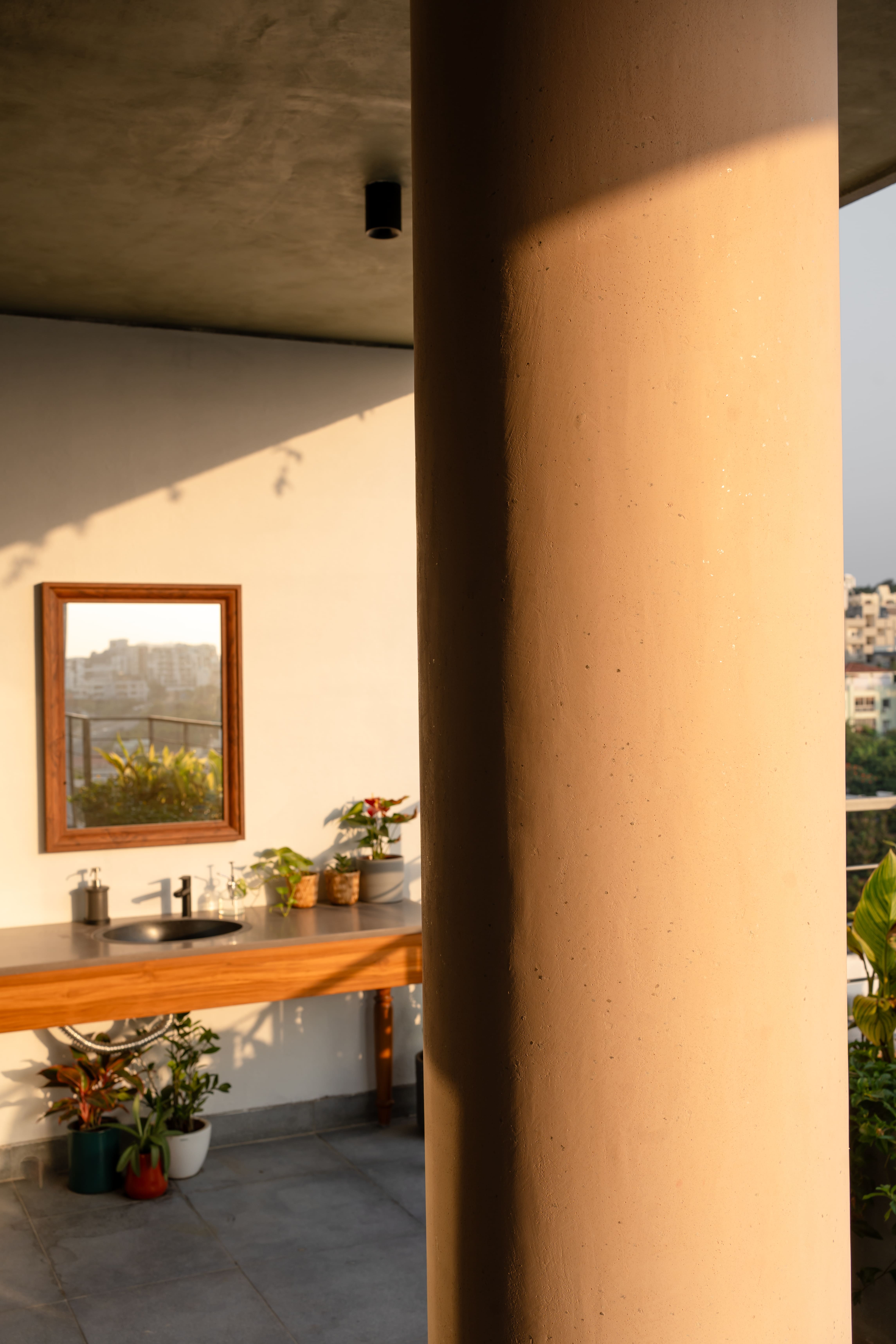 Balcony corner with wood-framed mirror, console basin and clustered terracotta planters in warm evening light, Hyderabad