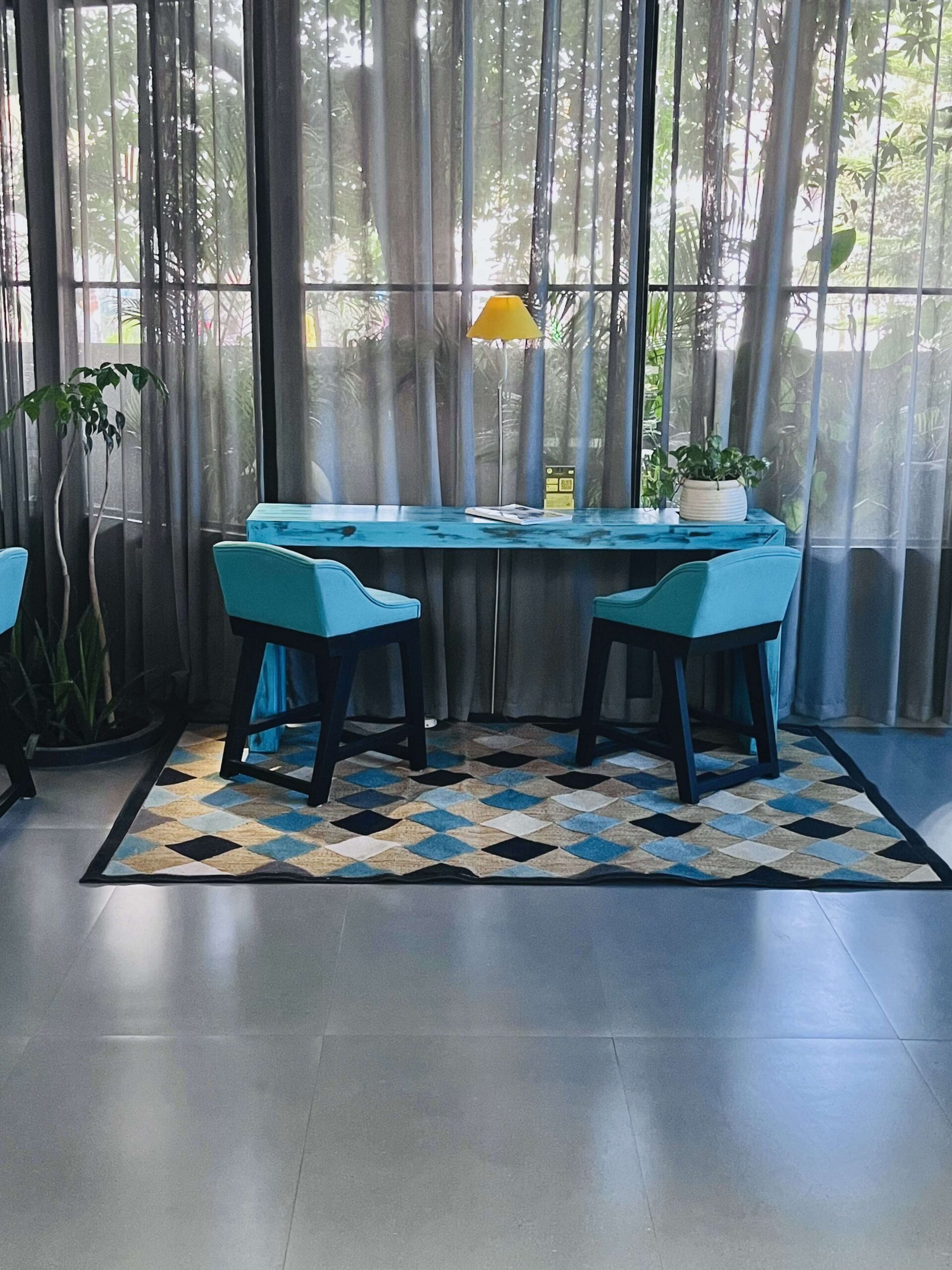 Breakfast nook with a turquoise table, teal chairs and a diamond-pattern rug beside sheer-curtained windows, Hyderabad