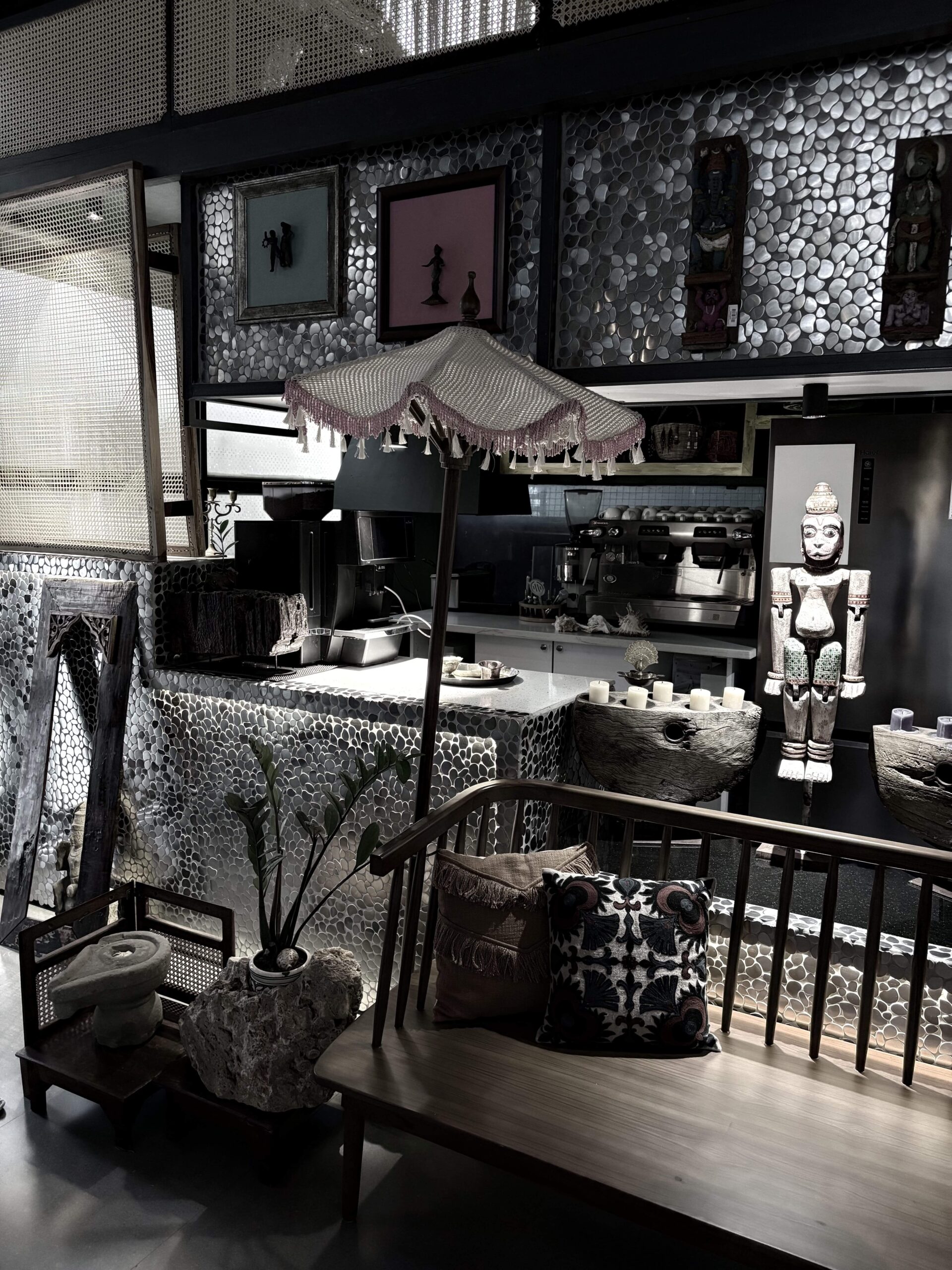 Dark eclectic lounge with pebble-mosaic walls, a fringed parasol lamp, carved figurines and a cushioned bench, Hyderabad
