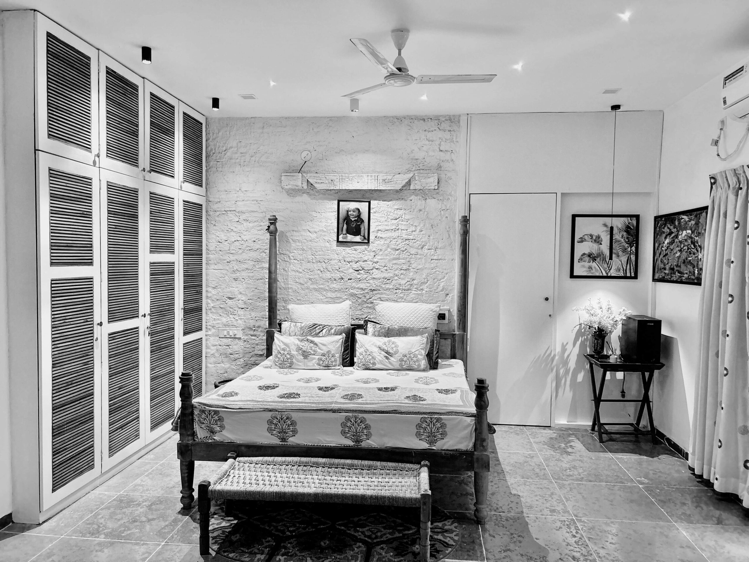 Black-and-white bedroom with a four-poster bed, block-print bedspread, louvered wardrobe and brick accent wall, Hyderabad