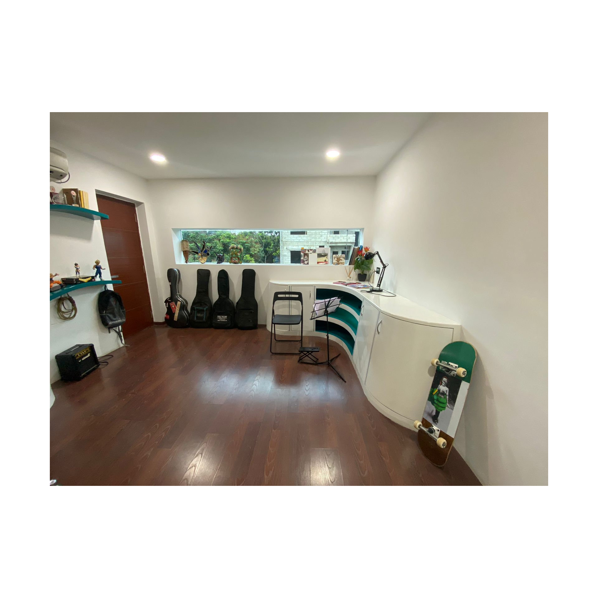 Music studio in Hyderabad with curved white desk, teal accents, guitar cases lined under window and dark wood floor