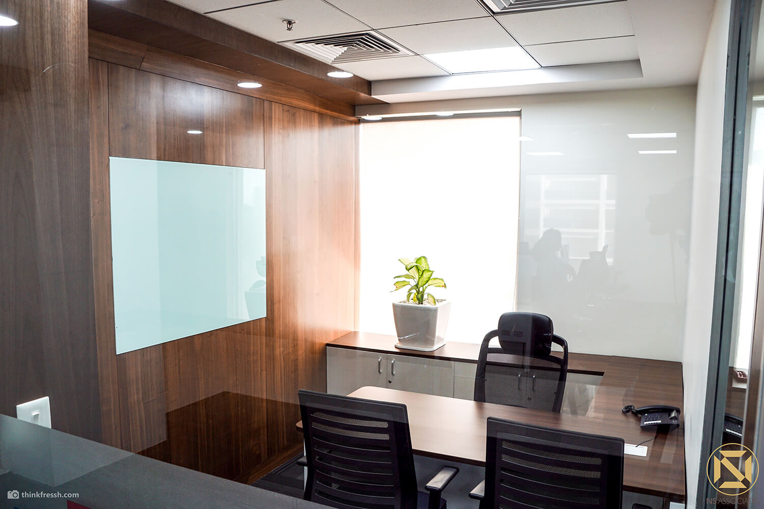 Small office cabin with wood-panelled wall, glass writing board, desk and black chairs, Hyderabad workplace