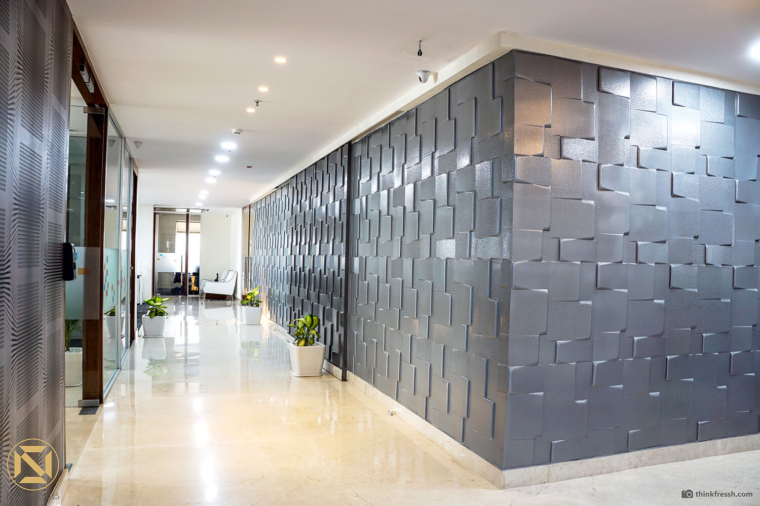 Office corridor in Hyderabad lined with a textured grey 3D tile feature wall and potted plants on glossy floors