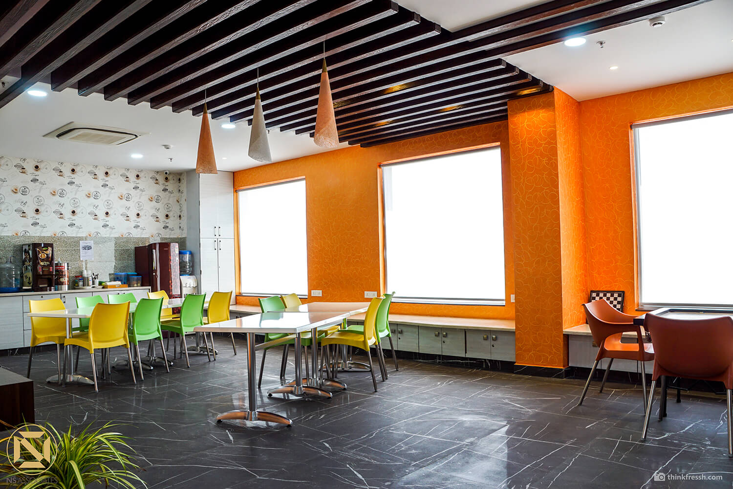 Office cafeteria in Hyderabad with orange walls, lime-and-yellow chairs, pendant lights and slate floor tiles