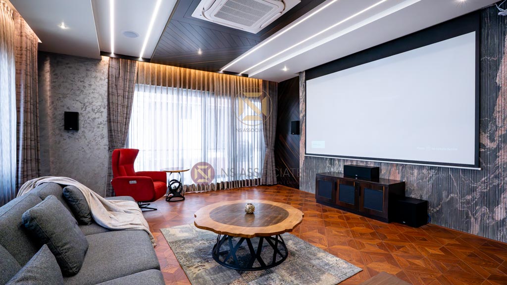 Home theatre room with large projection screen, grey sofa, red lounge chair and live-edge wood coffee table, Hyderabad