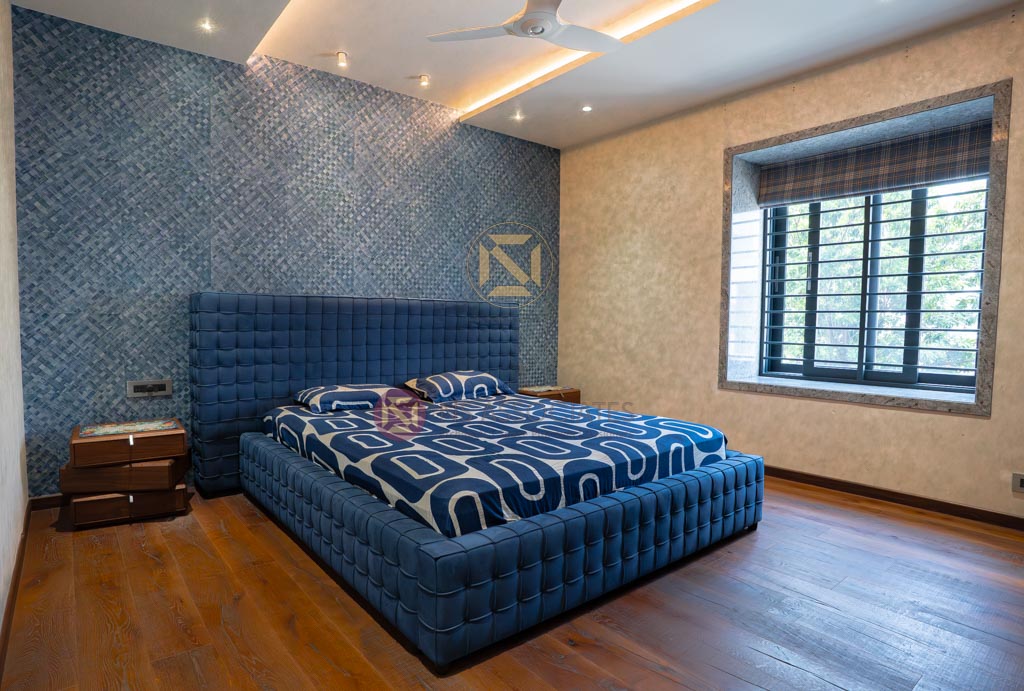 Bedroom featuring navy tufted bed, geometric blue accent wall and cove-lit false ceiling over wood floors, Hyderabad