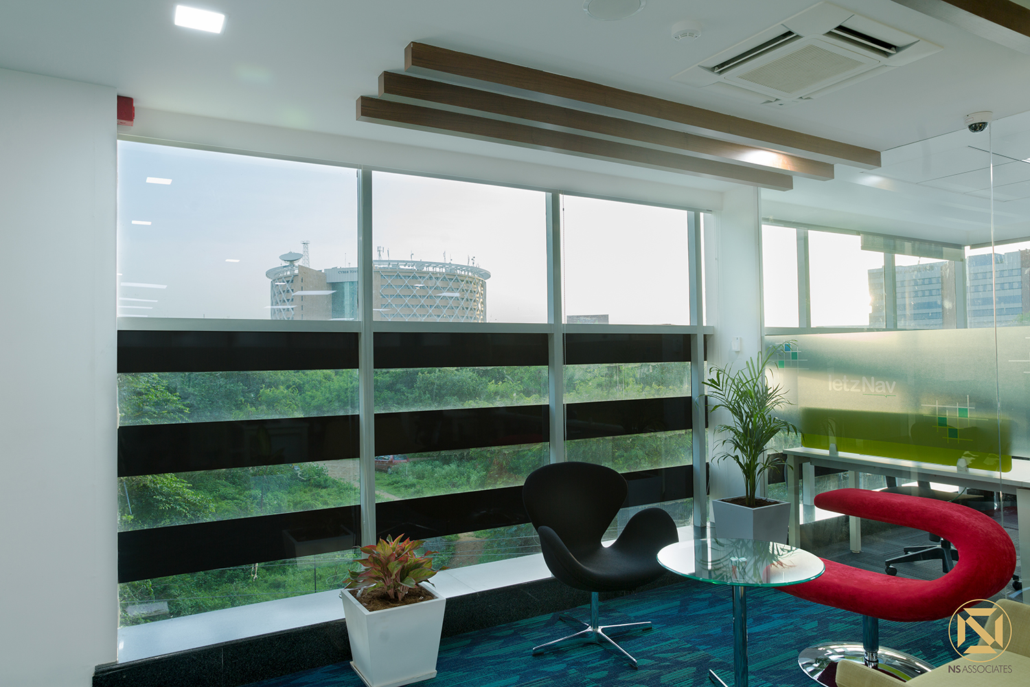 Breakout corner with black Swan chair, red lounge seat, glass table and panoramic city-view windows, Hyderabad