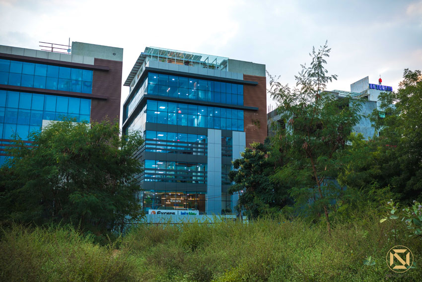 Glass-and-steel corporate office building exterior framed by greenery at dusk, Hyderabad