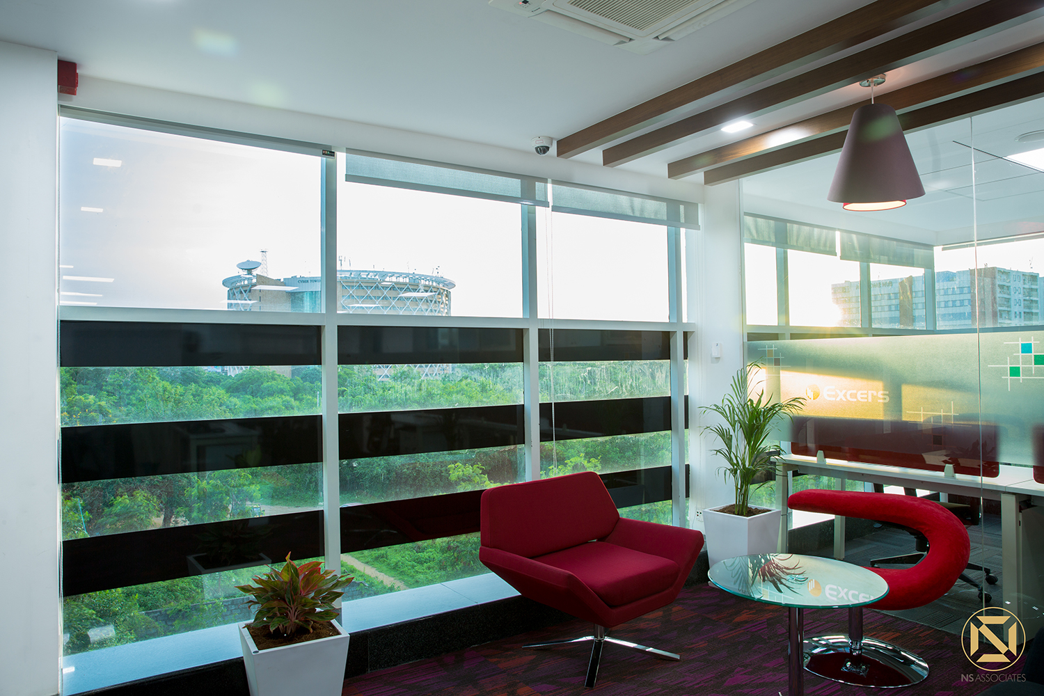 Office lounge area with red armchairs, pendant light and zebra blinds over wide glazing, Hyderabad