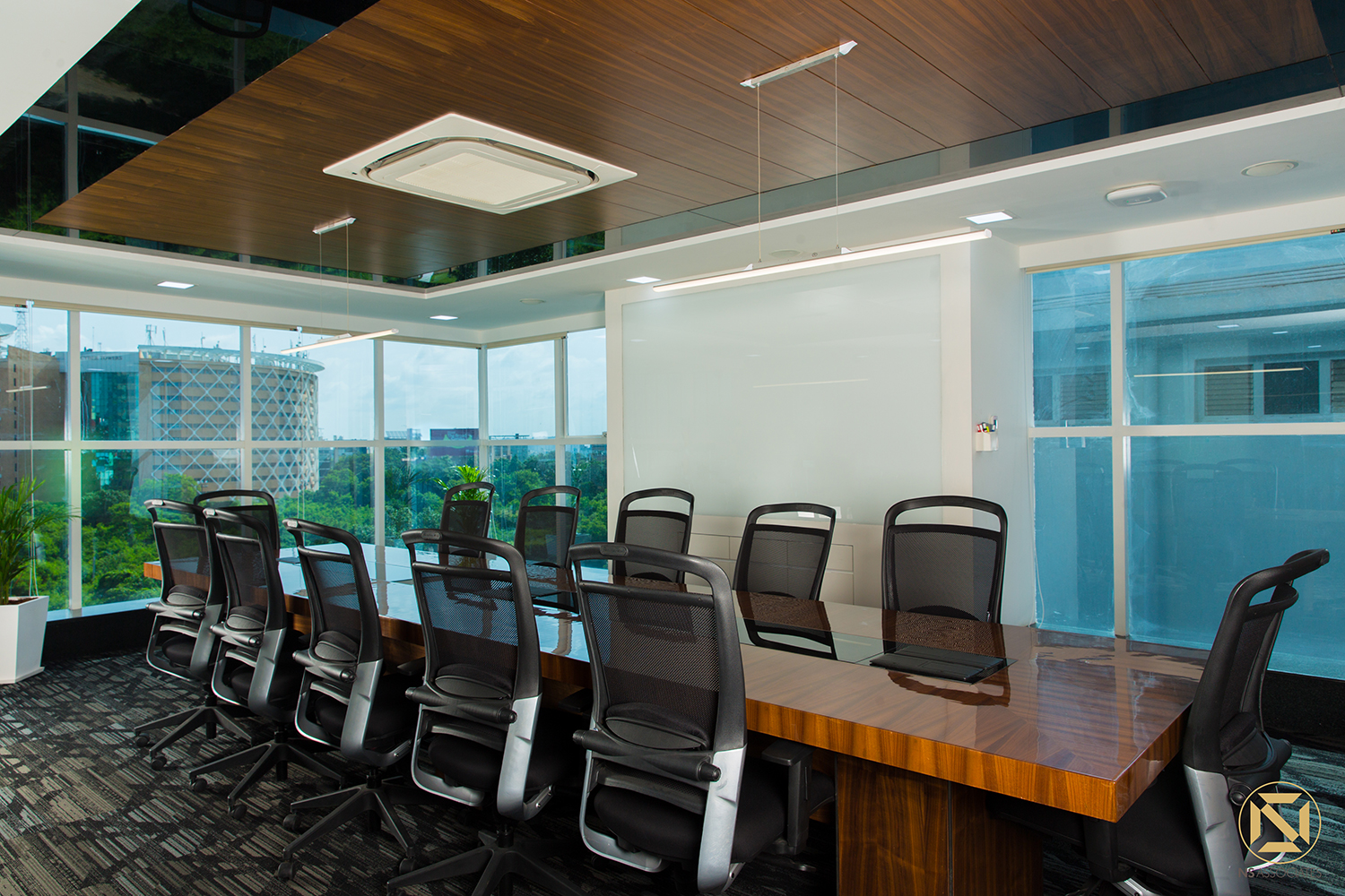 Corner boardroom with polished wood table, black ergonomic chairs and floor-to-ceiling windows over greenery, Hyderabad office