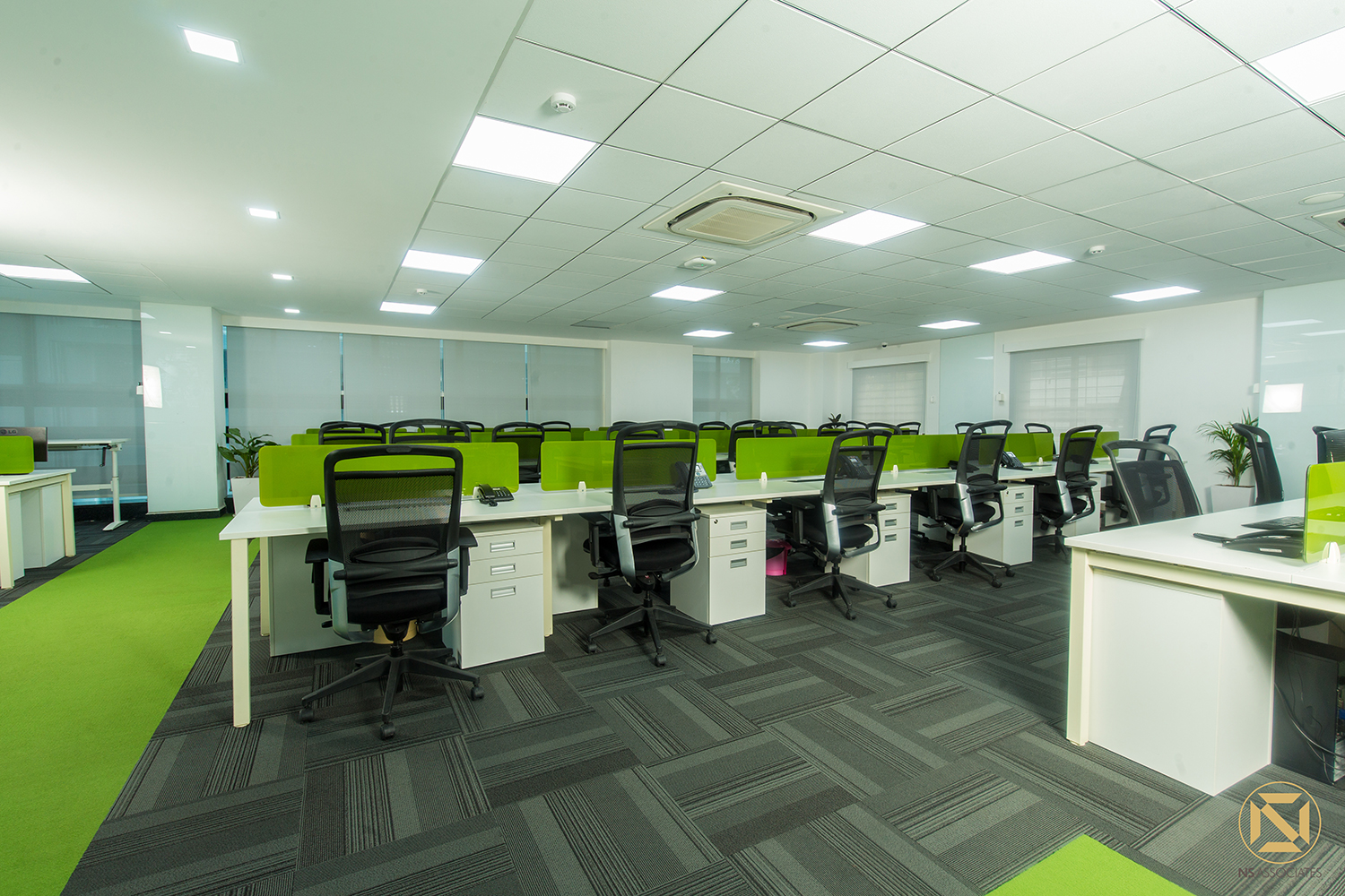 Open-plan office with white desks, lime-green privacy screens, black mesh chairs and grey carpet tiles, Hyderabad workspace