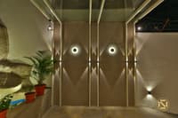 Textured taupe feature wall with recessed circular wall lights and potted palms in a Hyderabad home entryway courtyard
