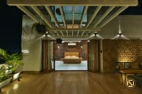 Wooden deck terrace under a pergola looking through glass doors to a brick-walled bedroom at night, Hyderabad full home