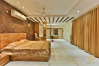 Bedroom with brown marble accent wall, wood-slat ceiling beams, golden bedspread and matching drapes, Hyderabad