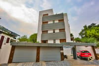 Four-storey residential building exterior with grey-and-white facade, roller-shutter garages and paver driveway, Hyderabad