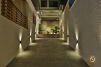 Outdoor entry passage at night lit by up-and-down wall lights, with potted plants against a rough stone niche, Hyderabad