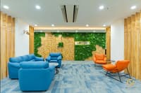 Office reception lounge with blue sofas, orange accent chairs and a green moss wall over wood, on blue carpet tiles, Hyderabad