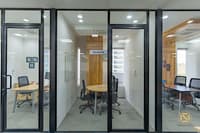 Corporate office cabins with black-framed glass partitions, wood accent wall and a round meeting table, Hyderabad