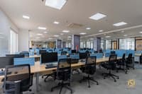 Large open office floor of desks with monitors, mesh chairs, blue dividers and branded columns, Hyderabad