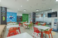 Staff breakout cafeteria with orange and green chairs, white tables, wellness wall posters and water dispenser, Hyderabad
