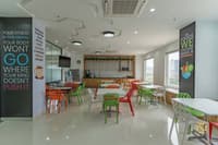 Office cafeteria with white tables, bright orange and green wire chairs, coffee counter and motivational wall graphics, Hyderabad
