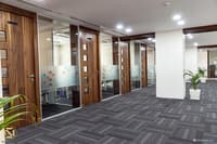 Office wing in Hyderabad with walnut-framed glass cabin doors, grey carpet tiles and white columns