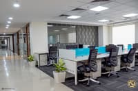 Open office bay in Hyderabad with white workstations, blue dividers, potted plants and a wave-textured accent wall