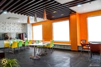 Office cafeteria in Hyderabad with orange walls, lime-and-yellow chairs, pendant lights and slate floor tiles