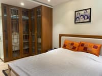 Bedroom corner with tall wood fretwork-and-glass wardrobes, upholstered headboard and orange patchwork pillows, Hyderabad