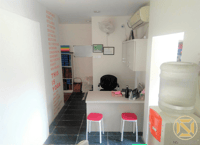 Compact office reception nook with desk, water dispenser and pink table with stools on tiled floor, Hyderabad