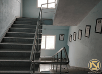 Stainless-steel stair with glass-railing landing and framed certificates on pale blue walls, Hyderabad office