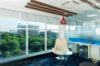 Breakout corner with cream tufted lounge chair, red pendant lamp and blue patterned carpet by panoramic windows, Hyderabad office