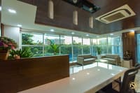 Office lounge with glossy white counter, wood-slat ceiling, pendant lights and grey sofas by a green garden view, Hyderabad