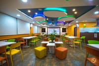 Office cafeteria with colourful chairs, circular LED-lit ceiling coves and orange accent walls, Hyderabad