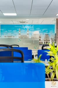 Office workstation with blue privacy panels facing a teal Hyderabad skyline mural of Charminar and Golconda, Excers Inc fit-out