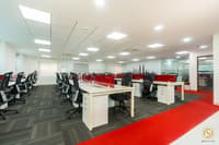 Open-plan office bay with rows of white workstations, red privacy screens and a bold red carpet runner, Hyderabad fit-out