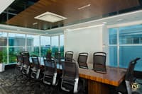 Corner boardroom with polished wood table, black ergonomic chairs and floor-to-ceiling windows over greenery, Hyderabad office