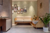 Office waiting nook with cushioned wood-frame sofa, cane bench, framed certificate wall and potted plant, Hyderabad
