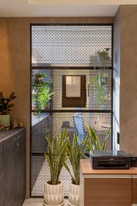 Office nook with black metal jali screen partition, microcement walls, snake plants in geometric planters and a printer console, Hyderabad