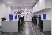Grey-marble workstation pods with blue dividers below a bold Auditing typography wall, Hyderabad office