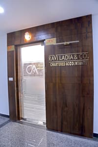 Walnut-clad office entrance with frosted glass door and gold Ravi Ladia & Co chartered accountants sign, Hyderabad