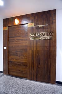 Office entrance with full-height teak wood-panelled wall and sliding door, brass signage for Ravi Ladia & Co Chartered Accountants, Hyderabad